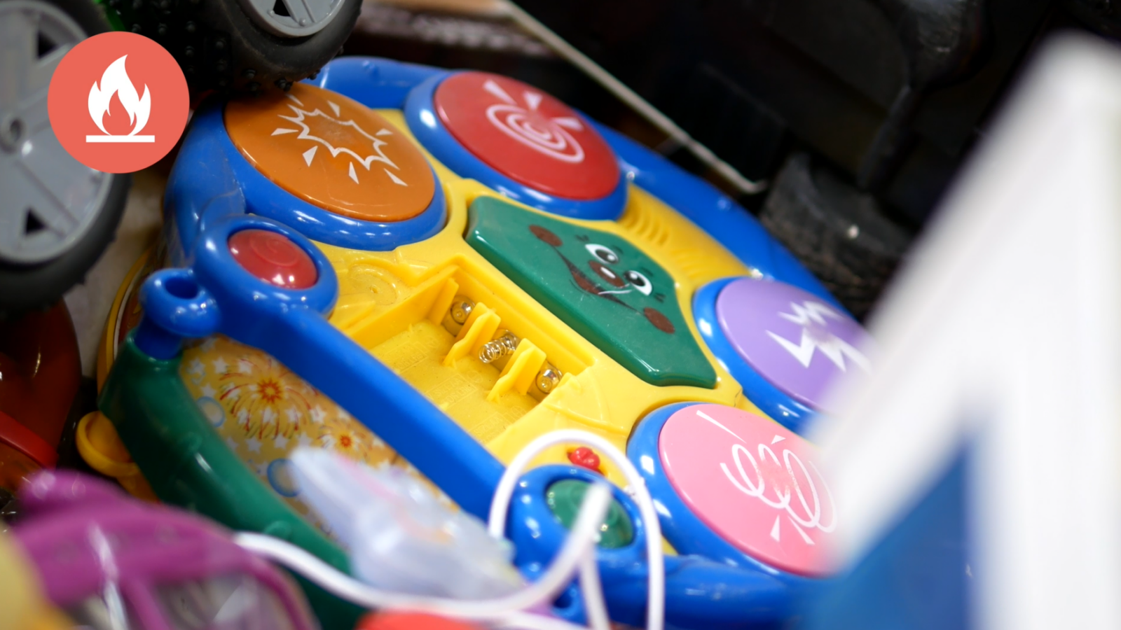 Jouet électrique à piles déposé par erreur dans une collecte de jouets non électriques, avec un pictogramme signalant le risque d’incendie.