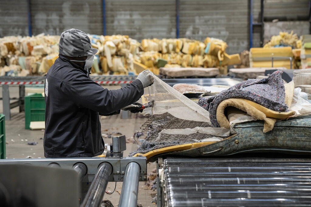 Opérateur retirant les différentes matières d'un matelas usagé sur une chaîne de démantèlement en vue de son recyclage.
